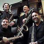 A photograph showing the Kessels saxophone quartet wearing black suits and smiling. 