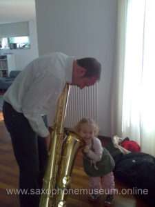 Photo of the bass saxophone and a child hugging it
